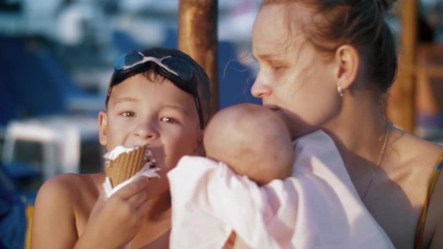 Slow motion shot of a boy eating waffle cone ice cream when relaxing at the beach with mum and baby sister