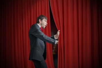 Curious actor or illusionist is looking behind red curtain and is surprised.