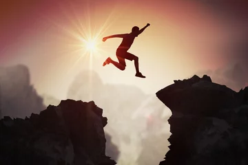 Foto op Plexiglas Silhouette of young man jumping over mountains and cliffs at sunset. © vchalup