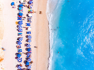 Fototapeta na wymiar Top down view of a beach with tourists suntbeds and umbrellas with sand beach and clear blue water in Greece
