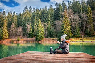 Happy young woman sitting on the wooden pier and drink coffee, m