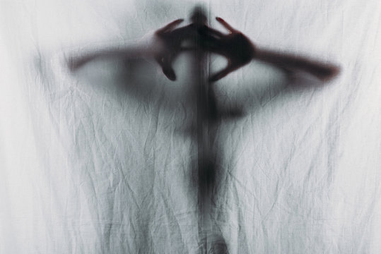 blurry silhouette of person touching curtain with hands