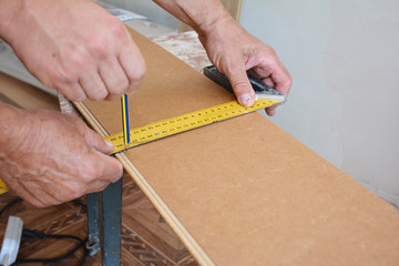 Fototapeta na wymiar Workers installing wooden laminate flooring and measuring laminate board before cutting.