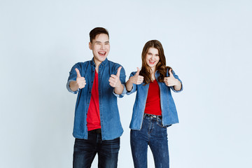 Portrait of happy young couple embracing on white background. The man and the woman showing thumb up sign with happy expression.