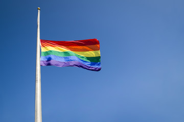 Gay pride rainbow flag flying at half mast in mourning on bright summer sun against blue sky