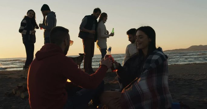 Group of young people having fun at beach around bonfire on sunset