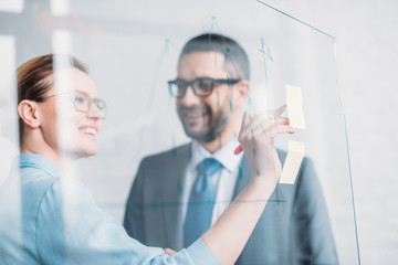 smiling business partners drawing graphs on glass presentation board