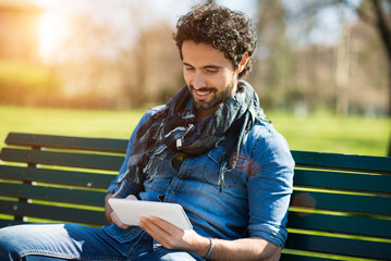 Smiling man using his tablet computer in a park