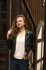 Fototapeta premium Fashionable blonde woman with bright makeup wearing leather jacket, posing at the street