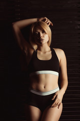 Adorable blonde woman in sport underwear posing in studio with shadow