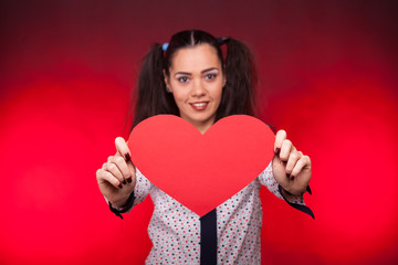 Woman holding a red papper heart in hands on dark red background