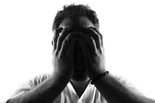 Male person silhouette crying and covering the face with the hands hiding the tears,back lit