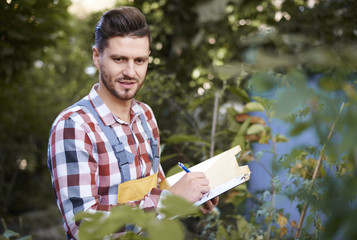 Man make notes on clipboard while checking flowers