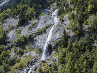 Fototapeta na wymiar Vista aerea di una cascata in Val di Mello, una valle verde circondata da montagne di granito e boschi, ribattezzata la Yosemite Valley italiana. Val Masino, Valtellina, Sondrio. Italia