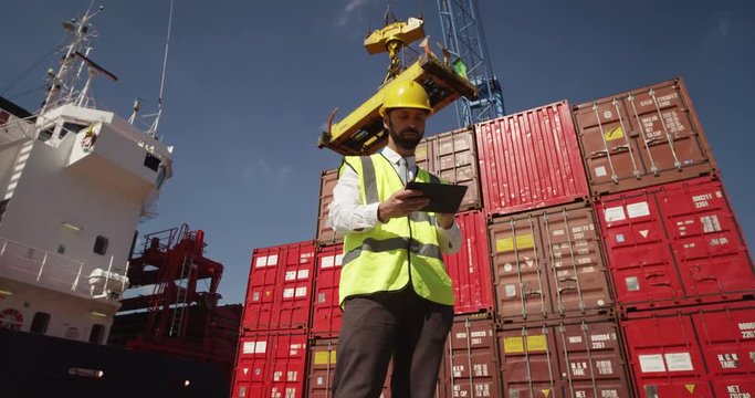A young manager doing inspection rounds through an industrial harbor working on a digital tablet. Shot on RED Epic.