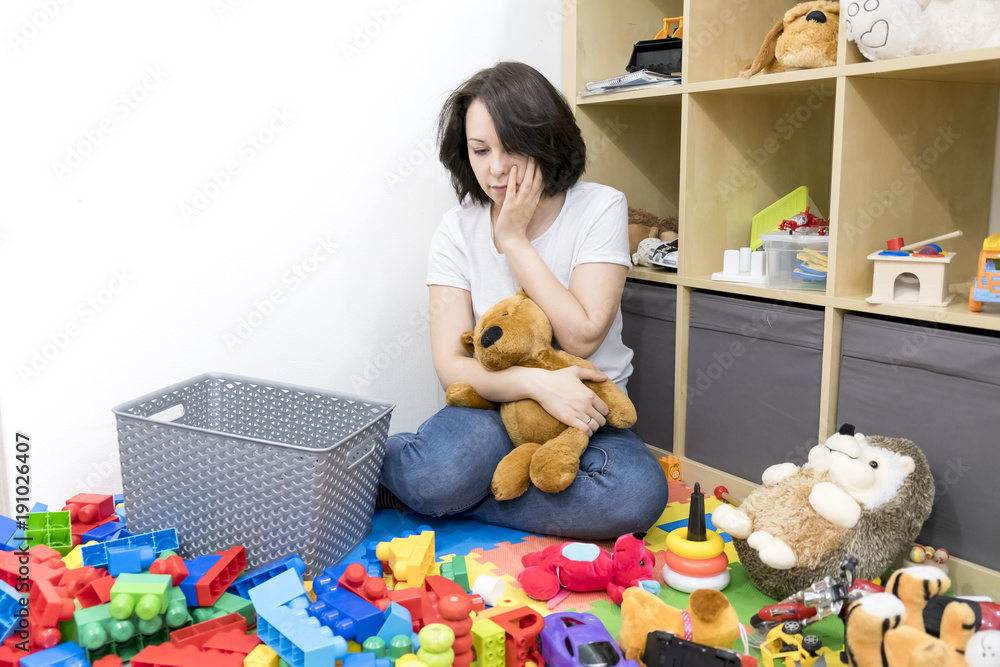 Wall mural young mother cleaning her kid's toys at home. woman tired after work. organization toy