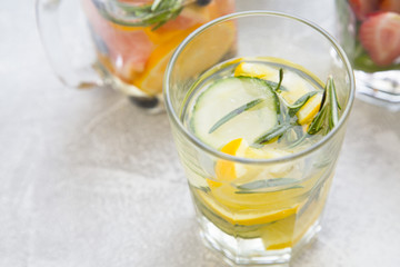 Glass of detox water with sliced lemon, cucumber and rosemary on light concrete background, close up