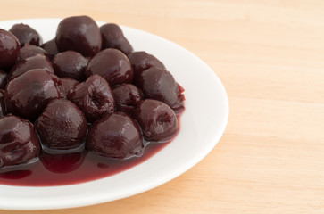 A serving of sweet pitted cherries on a white plate atop a wood table.