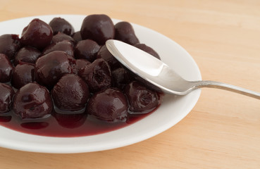 A plate of sweet pitted cherries with a spoon to the side on a wood table.