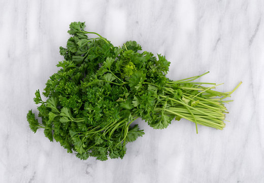 Top view of a bunch of curly parsley on a gray marble cutting board.