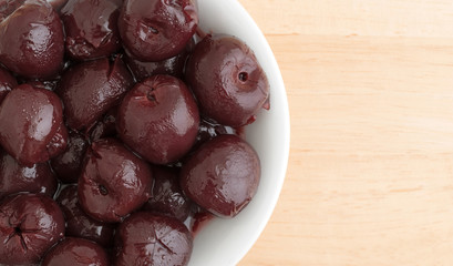 Top close view of a small white bowl of sweet pitted cherries on a wood table.