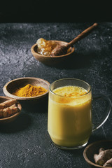Cup of ayurvedic drink golden milk turmeric latte with curcuma powder and ingredients above over black texture background. Toned image