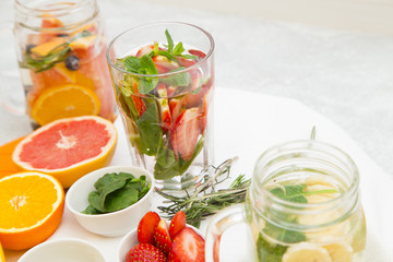 Glasses of detox water with sliced fruit, vegetables, berries and herbs, set of ingredients: banana, strawberry, orange, grapefruit, mint, white background