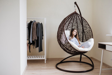 The girl sits in pajamas in a cocoon chair and reads a book. Stylish interior of the room.