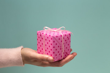 Woman's hand giving pink gift box in polka dots