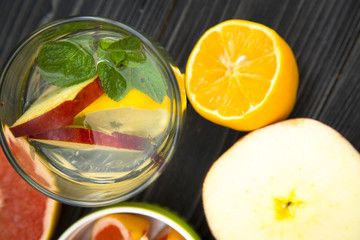 A glass of detox water with slices of fresh apple, lemon and a spring of mint, black wooden background, top view