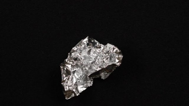 Sheet of aluminum foil is unfolding from the ball and again folds on a black background. Stop motion animation.