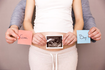 Pregnant woman with her husband holding ultrasound scan and blue and red post its with words boy or girl
