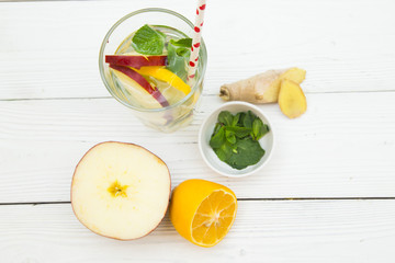A glass of detox water with sleces of fresh apple, lemin ginges and spinach with ingredients on white wooden table, top view