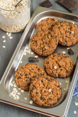 Delicious homemade pastries. Oatmeal cookies on a metal baking sheet and a glass jar with oat flakes on an old wooden table.