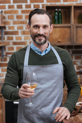smiling man holding glass of wine and looking at camera in kitchen