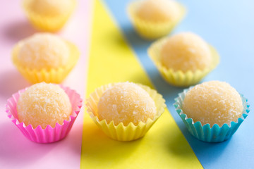 Beijinho is a candy from Brazil: condensed milk and coconut. Children brithday party sweet. Spread candy balls on colorful table. Design, selective focus.