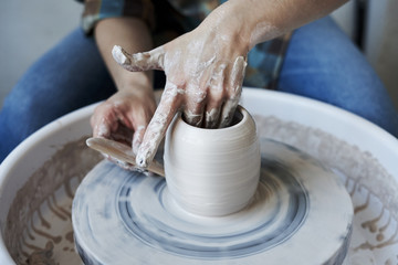 Fototapeta na wymiar Close-up of hands doing a pot or a vase in ceramic studio, craft working process with clay potter's wheel