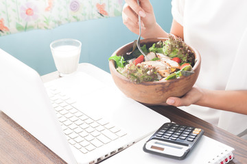 Woman hand holding salad bowl while working with laptop at home, Healthy lifestyle concept
