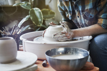 Ceramic studio, craft working process with clay potter's wheel, close-up of hands doing object