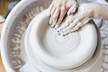 Ceramic studio, craft working process with clay potter's wheel, close-up of woman hands doing object