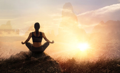 Woman practices meditating yoga on a stone, sunset mountains background