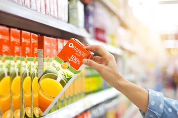 Crédence de cuisine en verre imprimé Jus Woman hand choosing to buy orange juice on shelves in supermarket