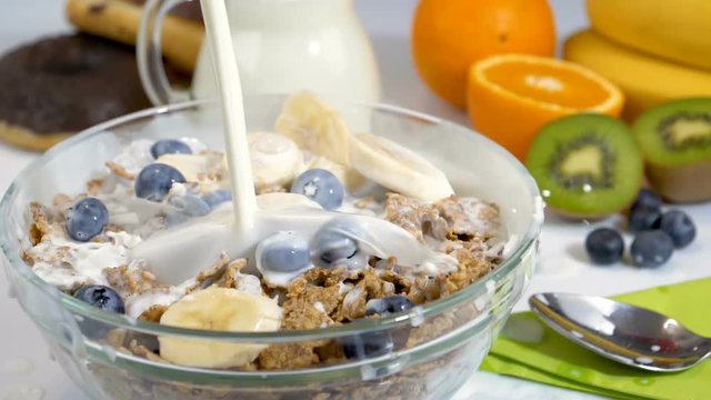 Pouring milk on cereals flakes and fruits for healthy and organic breakfast. Slow motion shot.