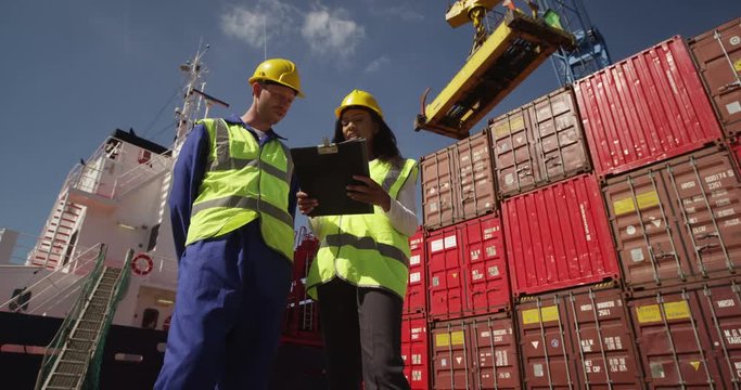 Businesswoman and dock worker shake hands at a busy shipyard. Shot on RED Epic.