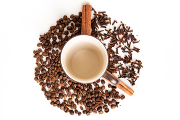 Top view of a coffee cup surrounded by coffee beans, cloves and cinnamon sticks forming a clock on white background.
