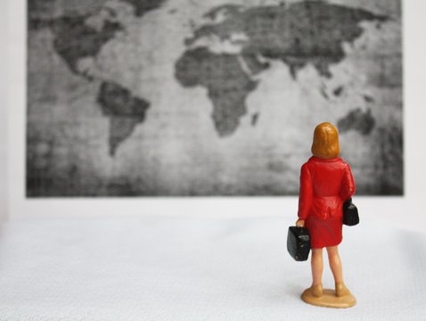 Miniature woman from behind on a business trip. Traveling around the world concept. Blurred black and white map of the worl background.