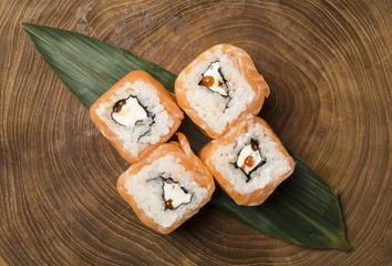 Top view of salmon homemade Philadelphia sushi rolls on wooden background with decorative leaf.