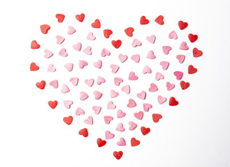 Small red and pink sugar hearts forming a big one on white background. Top view of valentine day’s symbol.