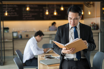 Asian businessman in black suit, who standing and holding document file about financial report on hand.