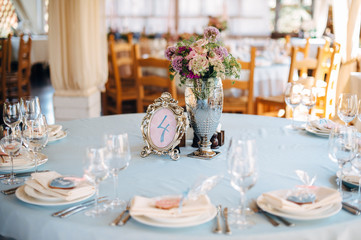 Decorated tables in sky-blue color with plates, knives, forks and bouquet in silver vase on the centre